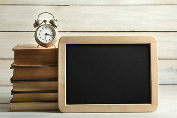 alarm clock with books and blackboard on wooden background