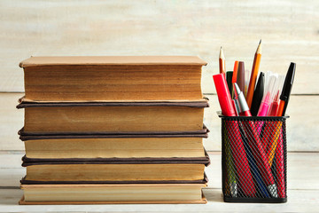 books near the pencil case for pens on wooden background