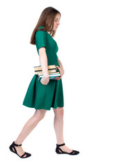 Girl comes with  stack of books. side view. Rear view people collection.  backside view of person.  Isolated over white background. The slender brunette in a green short dress sadly goes to the side