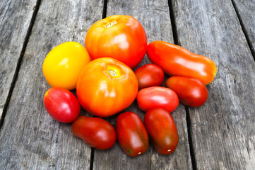 A few duferent colored tomatoes on the wooden deck