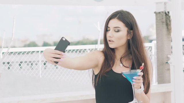 Young girl posing for selfie with goblet of blue cocktail on the beach