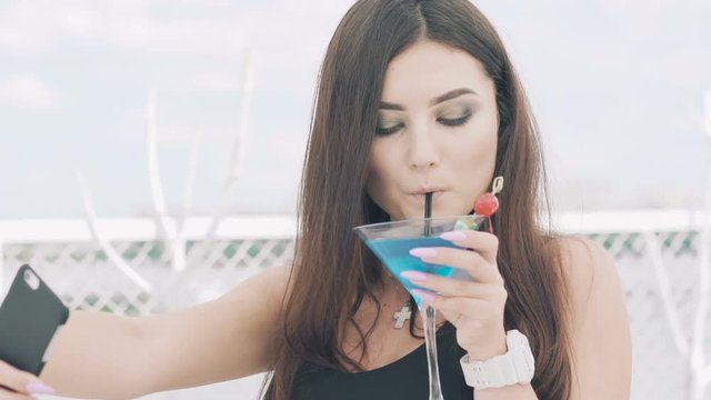 Young girl posing for selfie with goblet of blue cocktail on the pier