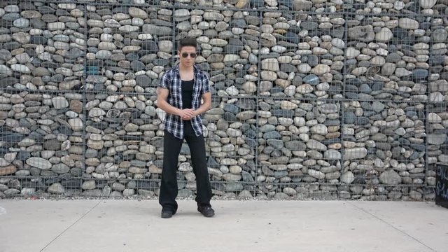 Young male trendy hip-hop dancer outside, doing break-dance in city setting in front of stone wall