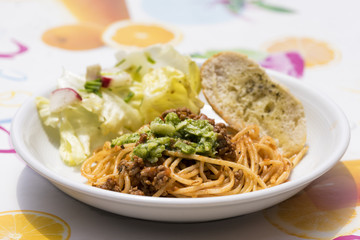 Close up on little round plate of pasta, bread slice and vegetables. Garnish of basil pesto on top of noodles.