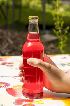 First Person Perspective View Of Hand Holding Red Colored Drink In Bottle Over Colorful Table Outdoors