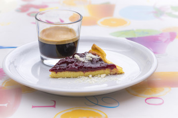 Single round ceramic white plate with espresso and red peach cheesecake wedge over colorful tablecloth