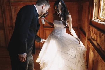 Groom looks at bride's dress while they stand in the hangar