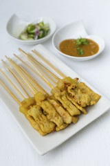 Pork satay on white plate with peanut sauce and cucumber salsa
