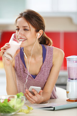 Woman drinking a healthy cocktail and listening to music in the kitchen