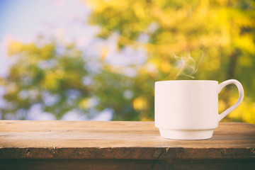 image of coffee cup over wooden table and tree leaves