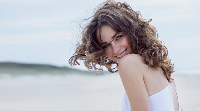 Красивая счастливая женщина на пляже. Портрет крупным планом. Фотография смеющейся  девушки на берегу моря. Ветер развевает волосы.