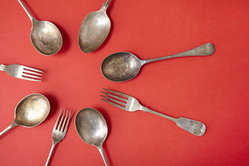 Old silver cutlery arranged in a circle on a red background
