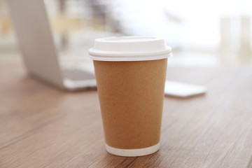 Paper cup of coffee on wooden table closeup