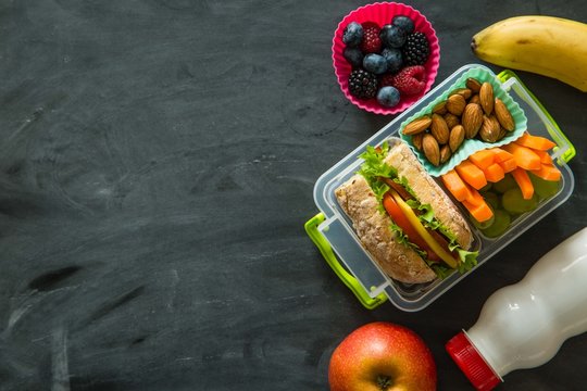 School lunch box with books and pencils in front of black board