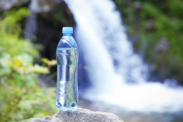 Bottle of clear water on blurred waterfall background