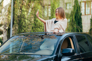 Picture of cheerful young woman wearing sunglasses and raised hands on the sunroof of the luxury car