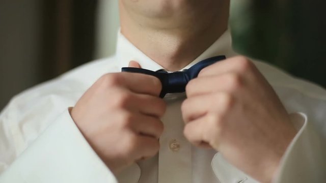 Close-up of young groom in white ivory shirt adjusting his bow tie