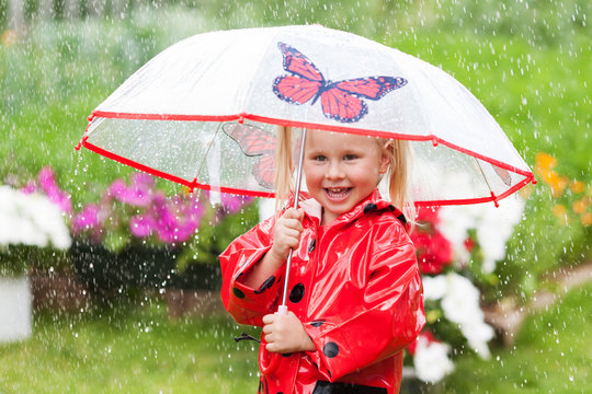 Happy fun pretty little girl in red raincoat with umbrella walking in park summer