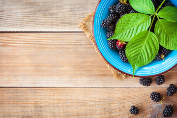 Fresh blackberries with leaves in blue ceramic bowl on wooden background in rustic style. Top view.