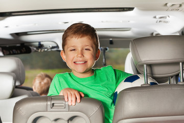 Happy kid boy sitting in the car and holding ball