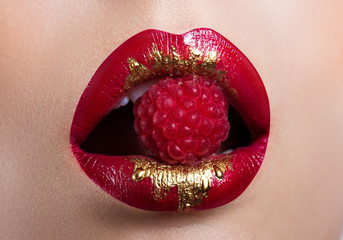 Naklejka premium Beautiful female lips closeup. Red lipstick with gold. Berry raspberry in mouth