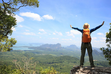 cheering successful woman backpacker open arms on mountain peak