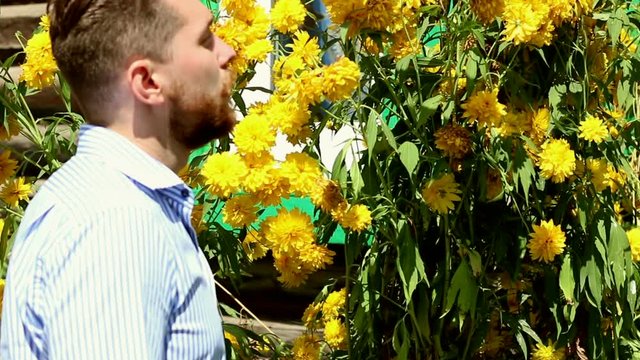 Young bearded man sniffing a flowers
