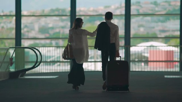 Business partners walking to airport escalator, carrying luggage, tourism
