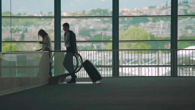 Business trip, man and woman walking to escalator in airport, carrying luggage