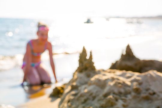 Blurred image of little girl playing with sandcastle at the sea front against of sun reflection. Greece