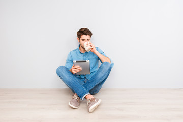Young man sitting on floor with crossed legs and tablet and drin