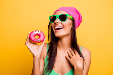 beautiful excited hipster girl in pink hat holding pink donut wi
