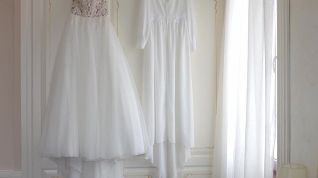 Wedding dress and cape hanging on hangers in the apartment