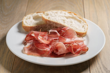 speck slices on white plate with ciabatta on old wood table