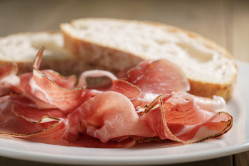 speck slices on white plate with ciabatta on old wood table