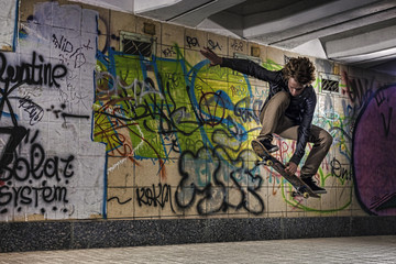Skateboarder doing a skateboard trick against graffiti wall