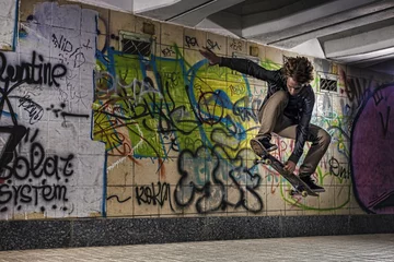 Tuinposter Skateboarder doing a skateboard trick against graffiti wall © 27mistral