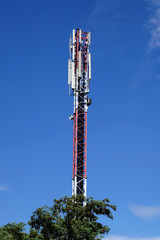Mobilfunkantenne (Handymast) mit Baum vor blauem Hintergrund (Himmel)