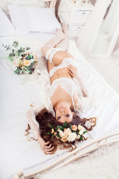 Sexy bride with bouquet lying at the morning on a bed dressed in white nighty and wreath. top view. Horizontal. Image released.