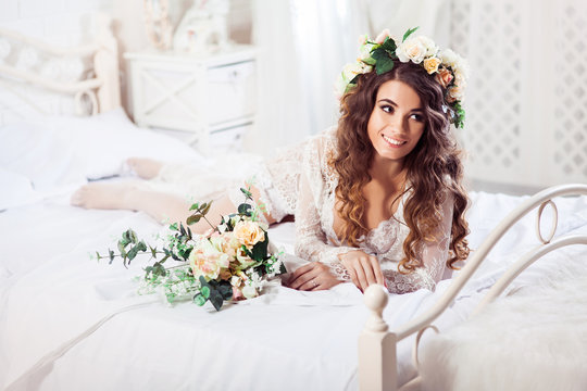 Sexy bride with bouquet lying at the morning on a bed dressed in white nighty and wreath. Horizontal. Image released.