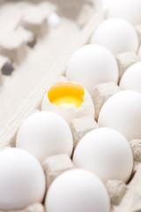 a dozen fresh, free range, white, organic eggs in carton. one broken with selective focus, close up, vertical