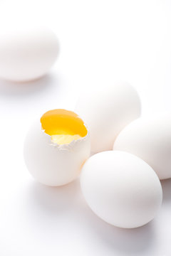 five fresh, free range, white, organic eggs. one broken with selective focus, close up, isolated on white background and vertical