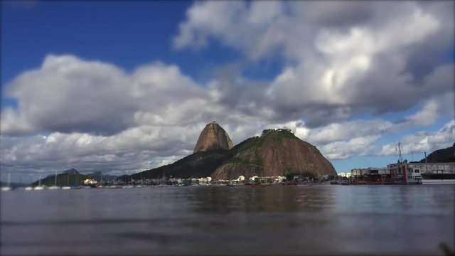 Clouds move in timelapse across classic view of Pao de Acucar Sugarloaf Mountain in Rio de Janeiro, Brazil standing above Guanabara Bay from the shore of Botafogo Beach