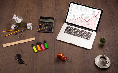 Computer desk with laptop and red arrow chart in screen
