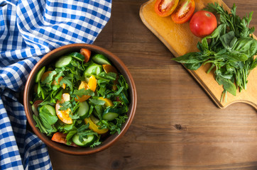A large portion of salad with fresh basil leaves, arugula, parsley, tomatoes. On a wooden table with a tablecloth. Top view