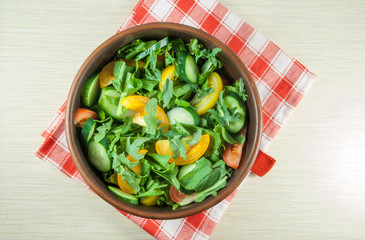 A large portion of salad with fresh basil leaves, arugula, parsley, tomatoes. On a wooden table with a tablecloth. Top view