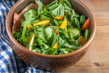 A large portion of salad with fresh basil leaves, arugula, parsley, tomatoes. On a wooden table with a tablecloth. 