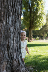 Portrait of happy little girl looking at camera while hiding behind tree trunk