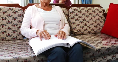Senior woman reading book in braille in retired house - Powered by Adobe