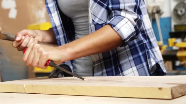 Focus on carpenter using hammer and chisel on a wooden plank